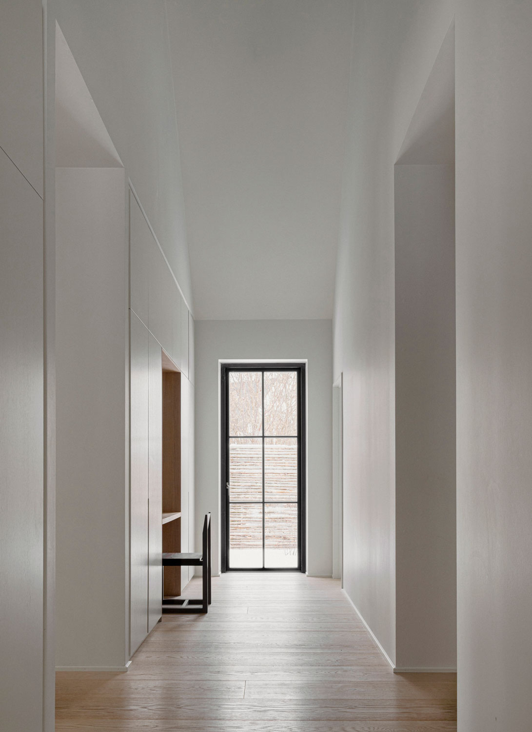 Minimal lake house interior hallway with daylight and a bathroom axis beyond