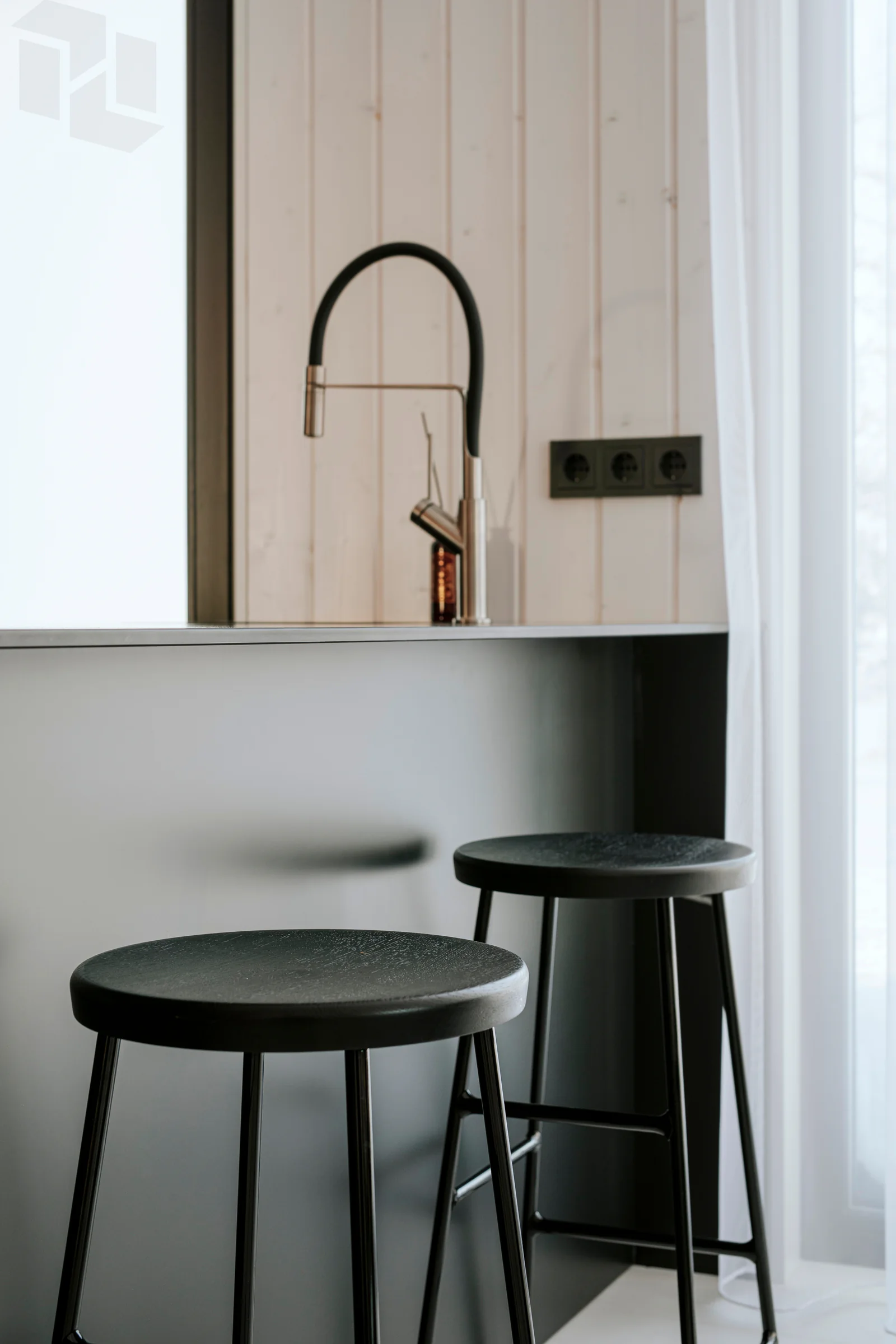 Kitchen detail with black counter, pale wood paneling, stools, and soft window light