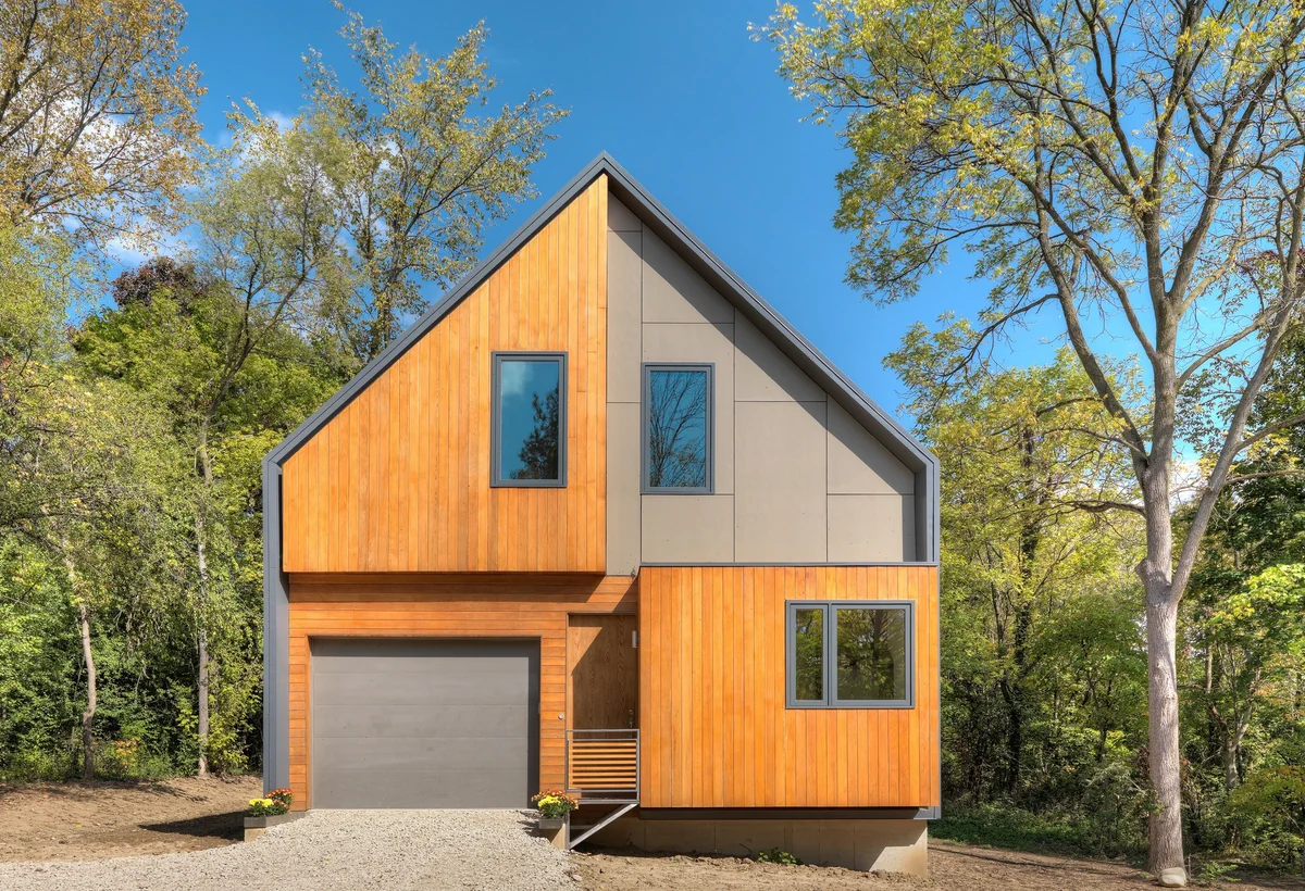 Modern home with warm wood gable, dark frame, trees, and broad roof planes