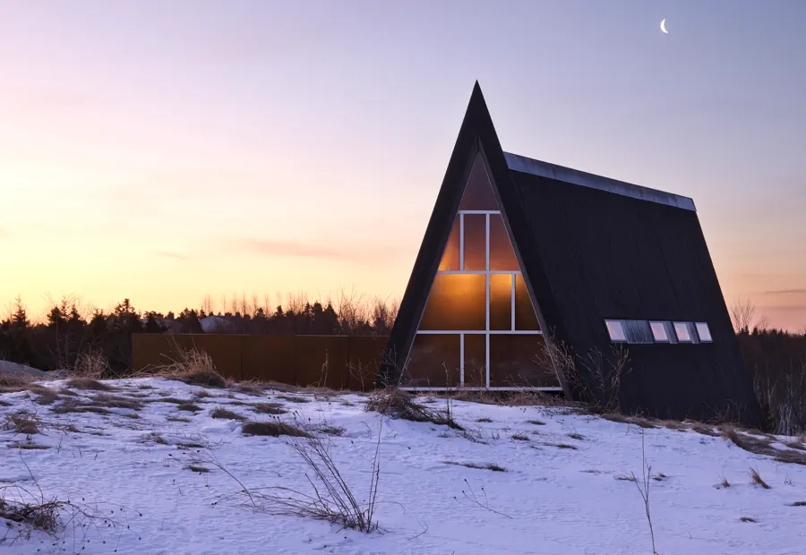 A-frame cabin in winter snow with a dark roof and warm glass gable