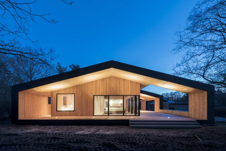 Wood-clad home with a dark roof frame and covered outdoor room at evening