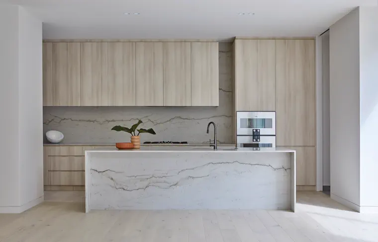 Bright kitchen with stone island, warm wood cabinetry, and open living area