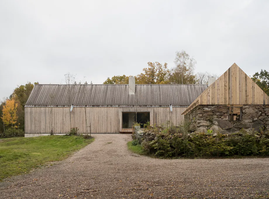 Wood-clad home with gravel access, stone retaining wall, and pitched rooflines
