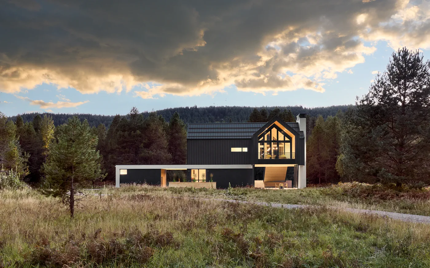 Wooded home with standing-seam metal roof, warm glass gable, and stormy sky